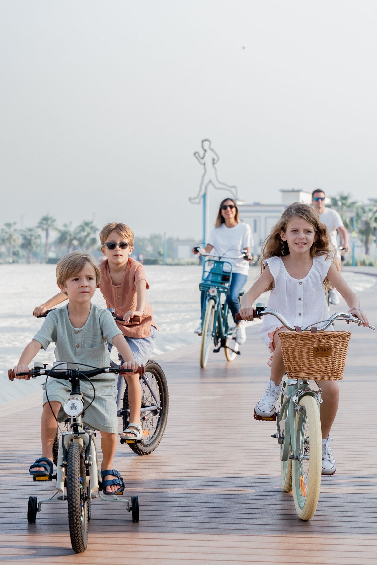 Children riding bicycles with adults in the background on a boardwalk.
