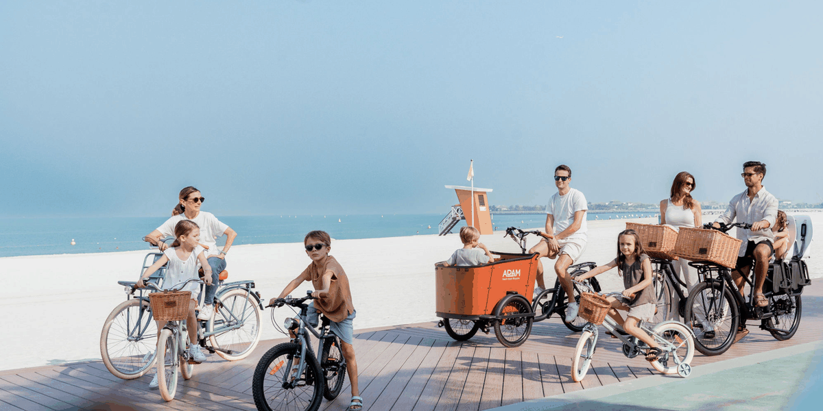 Families riding Adam bikes and an Adam cargo bike on a Dubai beach boardwalk